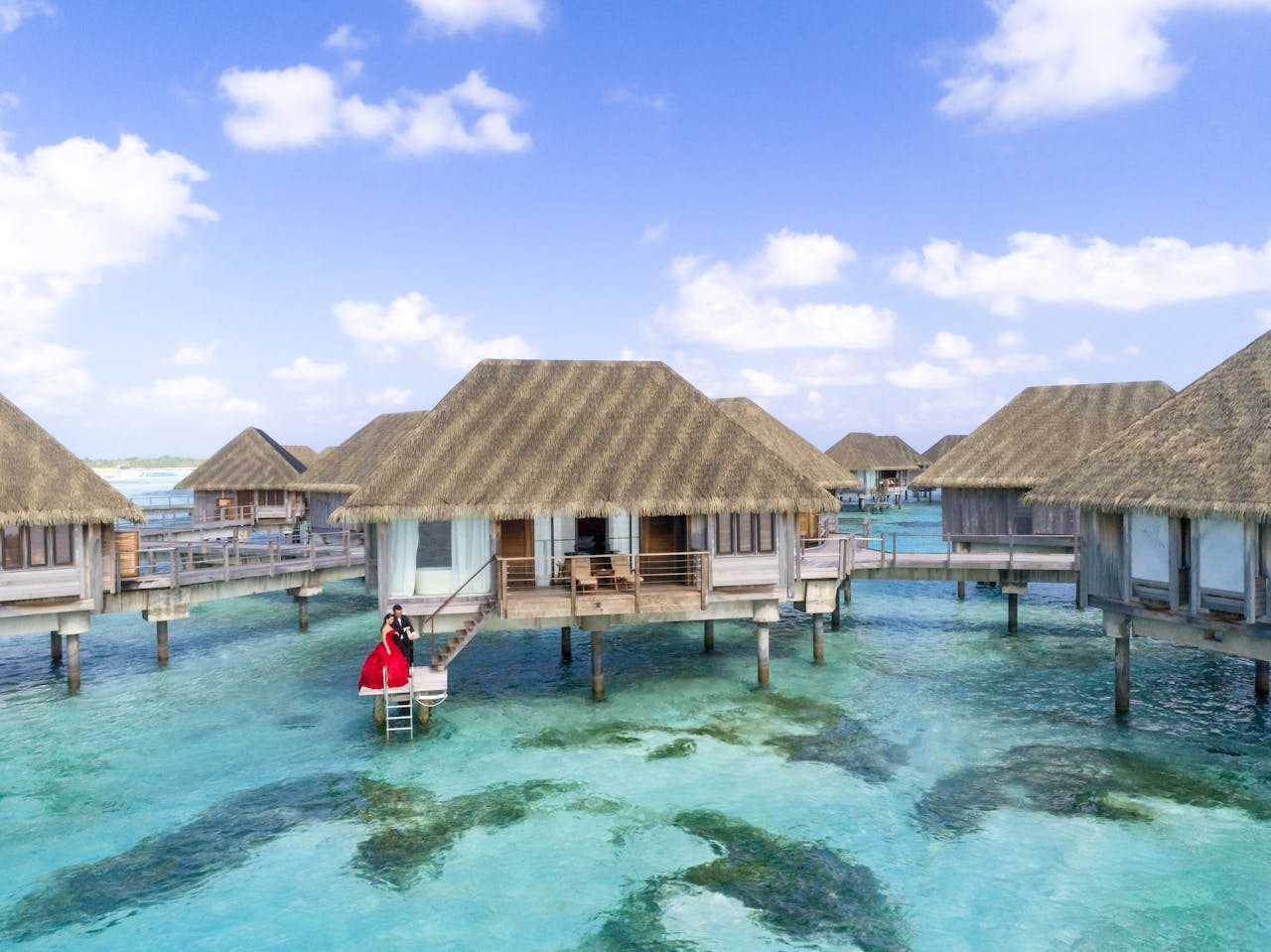 gallery-4 Overwater villa with couple in red dress in a tropical paradise setting.