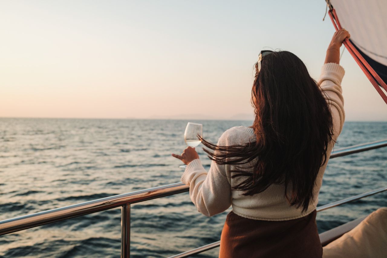 services-03 A woman with long brunette hair enjoys a drink while sailing at sunset.