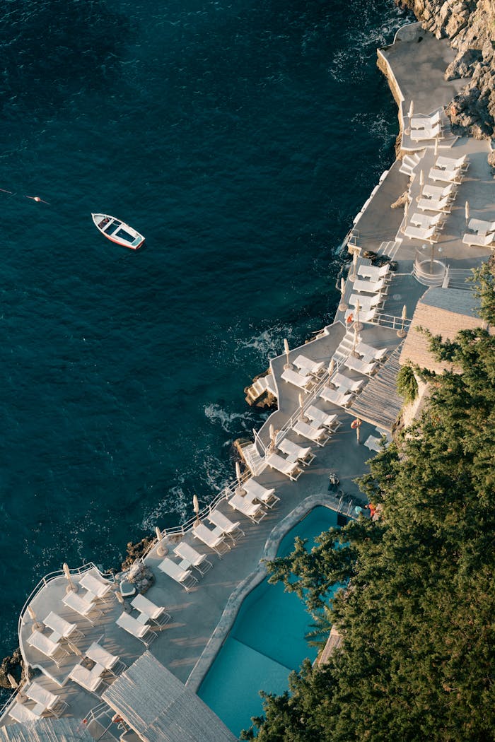 contact-img Aerial shot of a coastal resort with lounging area and small boat in the ocean.